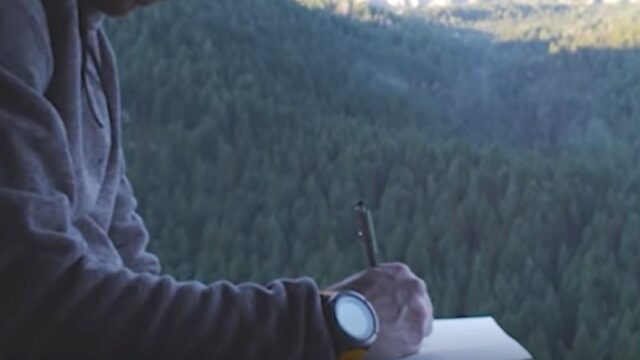 a person holding a pen and looking at a forest- relojes de montaña